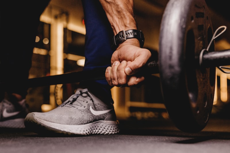 A person catching their breath beside a loaded barbell in a sunlit gym